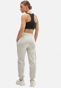 Top corto negro sin mangas con tirantes amplios, combinado con pantalones de chándal gris claro y ajustados que cuentan con bolsillos laterales y cinturilla elástica.