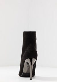 Czarne zamszowe botki za kostkę o eleganckim kształcie, z wysokim metalicznym obcasem i detalem w postaci zamka z tyłu. Gładka faktura i nowoczesny design.