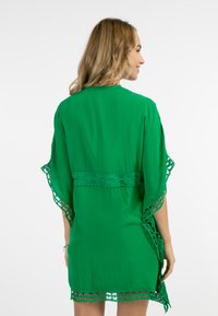 Zeleni kimono plašč s čipkastim okrasjem ob rokavih in robu. Gladko blago z odprtim hrbtom in širokimi rokavi.