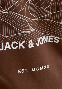 T-shirt en coton marron avec un design en art linéaire blanc représentant des formes de montagnes. Texte imprimé : "JACK & JONES" et "EST. MCMXC".