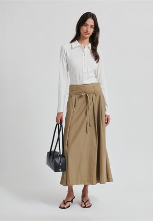 Top blanco de manga larga con textura acanalada y cierre de botones, combinado con una falda beige, fluida y de talle alto, sujetada con un bolso negro.