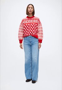 Suéter de punto rojo con patrón de corazones y diseño de "XOXO", combinado con jeans de pierna ancha en azul claro y zapatos negros. Look simple y acogedor.