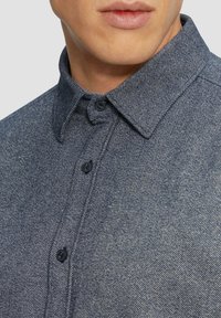 Donkerblauw, geweven overhemden met kraag en zwarte knopen. Close-up beeld dat de stofweefsel en detail van de sluiting benadrukt.