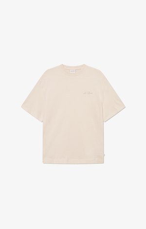 T-shirt de algodão bege com um corte solto, mangas curtas, decote redondo e uma marcação discreta no peito. Textura suave, design minimalista.