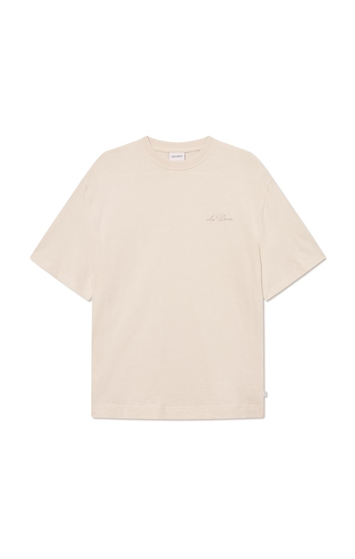 Beige bavlněné tričko s volným střihem, krátkými rukávy, kulatým výstřihem a decentním logem na hrudi. Hladká textura, minimalistický design.