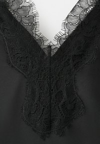 Tissu noir avec une bordure en dentelle florale délicate formant un décolleté en V avec des bords festonnés délicats.