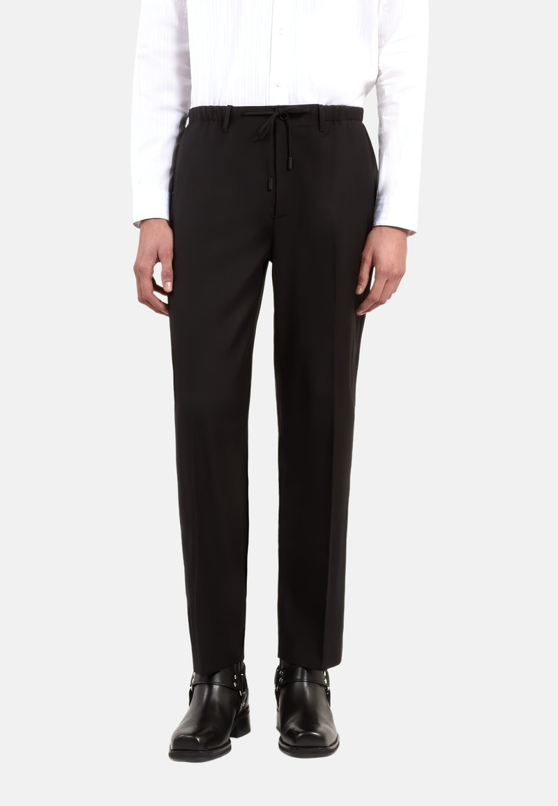 Zwarte op maat gemaakte broek met een elastische koordtailleband, een gladde textuur, een taps toelopende pasvorm en gedragen met zwarte enkellaarsjes.