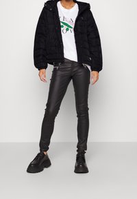 Czarna kurtka puchowa z kapturem, biała koszulka z grafiką i kolorowymi akcentami, czarne skórzane spodnie skinny oraz masywne czarne buty.