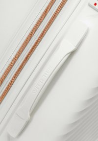 Maleta rígida blanca con superficie texturizada, cremallera en tono oro rosa y asa moldeada marcada con "WITTCHEN". Presenta un diseño aerodinámico.