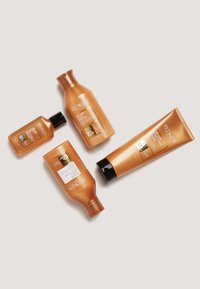 Quatre produits de soins capillaires Redken dans des bouteilles de couleur ambre : deux shampoings, un après-shampoing et un traitement, avec des étiquettes aux accents dorés.