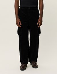 Schwarze Corduroy Cargohosen mit lockerem Schnitt, ausgestattet mit seitlichen Taschen und einer strukturierten Oberfläche. Tragen mit braunen Schnürschuhen.