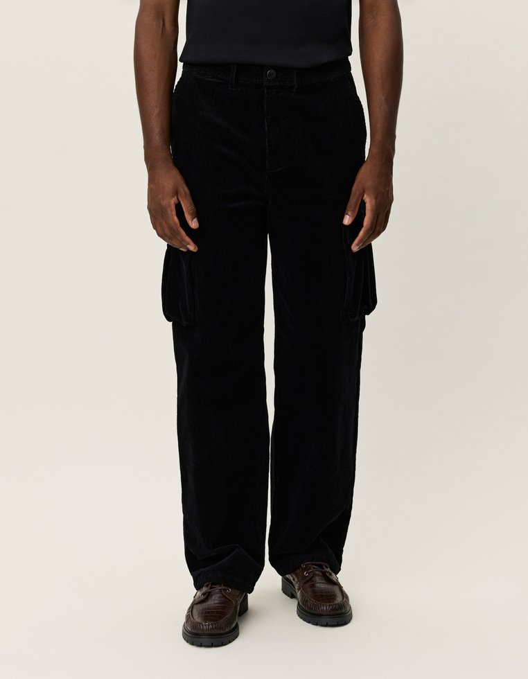 Schwarze Corduroy Cargohosen mit lockerem Schnitt, ausgestattet mit seitlichen Taschen und einer strukturierten Oberfläche. Tragen mit braunen Schnürschuhen.