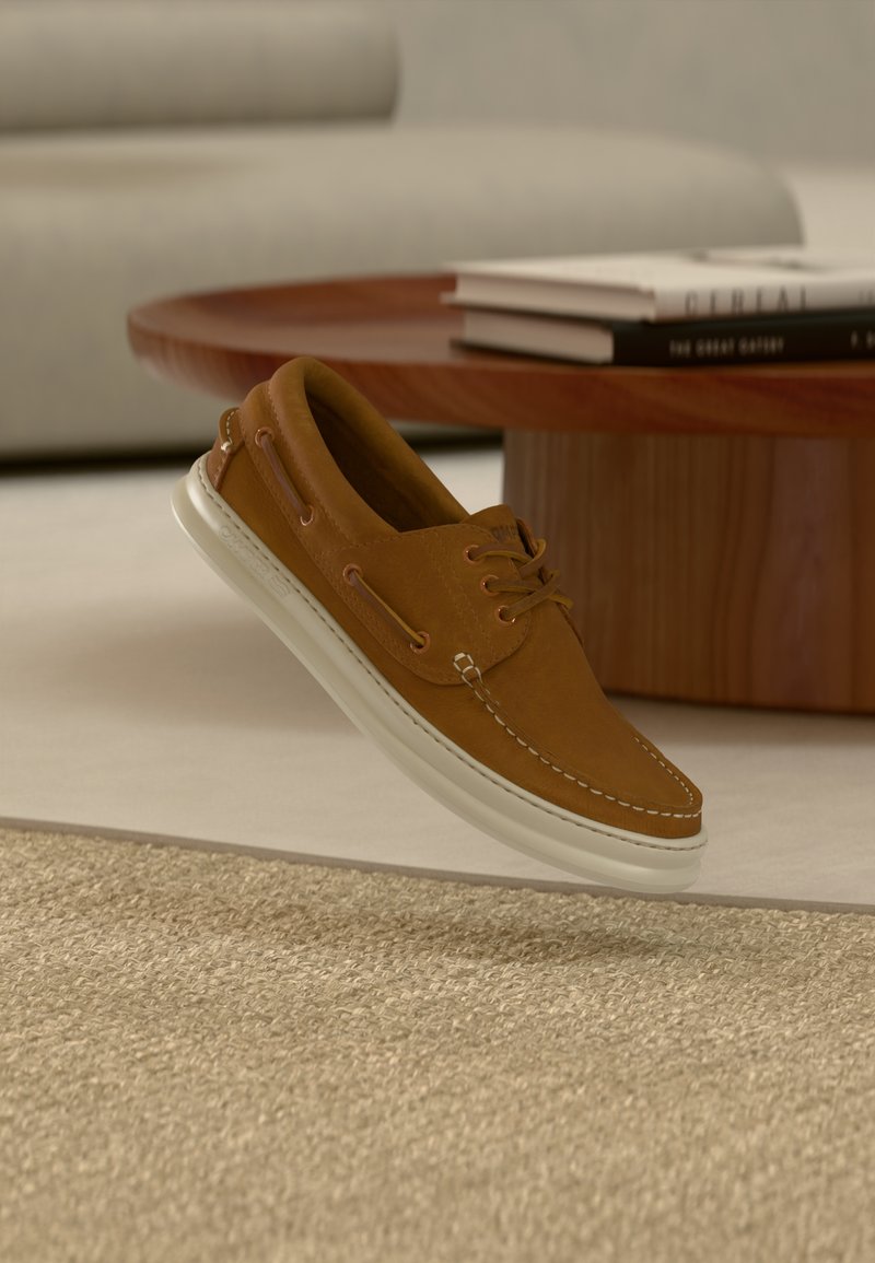 Chaussure bateau en cuir marron avec semelle en caoutchouc blanche, présentant des détails cousus, un laçage à l'avant et des œillets en métal.