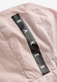 Hellrosa Stoff zeigt ein schwarzes, vertikales, rechteckiges Panel mit dem Wort „BAKER“ in weißen Buchstaben, das eine glatte Textur und ein minimalistisches Design präsentiert.