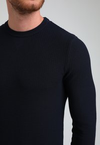 Granatowy sweter dzianinowy z textured wzorem, okrągłym dekoltem i długimi rękawami, wykonany z elastycznego materiału, co zapewnia dopasowany wygląd.
