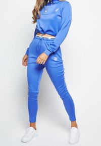 Blaue Sportbekleidung bestehend aus einem Sweatshirt mit Reißverschluss am Hals und passgenauen Jogginghosen, aus glatt verarbeitetem Stoff mit Zugbandbund und Logodetails.