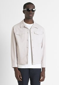 Lichtgrijze jacket van glad materiaal, met een puntige kraag, twee borstzakken en drukknoopsluitingen. Draag het over een wit overhemd.