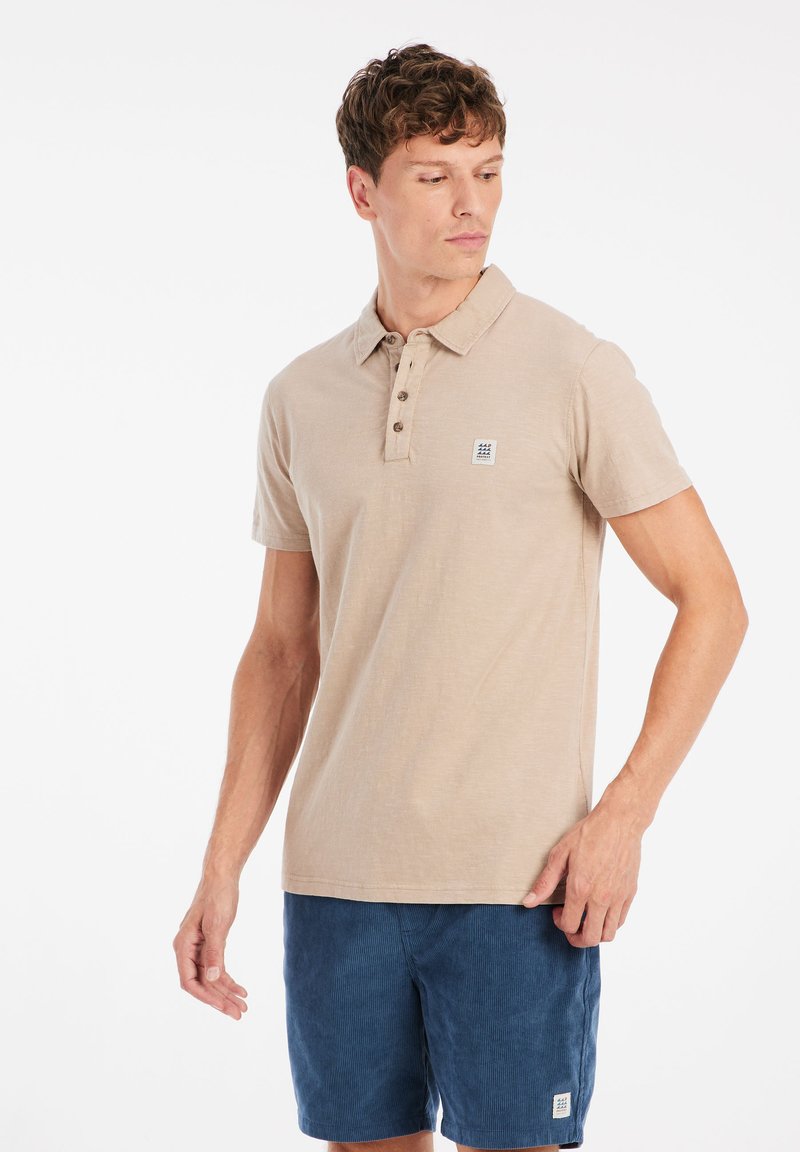Beige polo shirt met korte mouwen en een kraag, drie-knopen sluiting en een klein logo label; gecombineerd met marineblauwe corduroy shorts.
