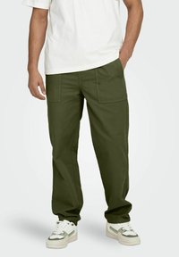 Pantalons cargo vert olive avec une coupe décontractée, dotés de deux poches avant et d'ourlets resserrés, associés à des chaussures de sport blanches.