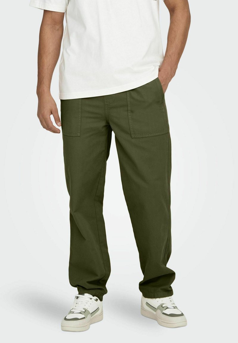 Pantalons cargo vert olive avec une coupe décontractée, dotés de deux poches avant et d'ourlets resserrés, associés à des chaussures de sport blanches.