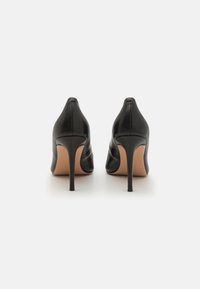 Černé kožené boty na vysokém podpatku s špičatou špičkou, s hladkým povrchem a štíhlými stiletto podpatky, na bílém pozadí.