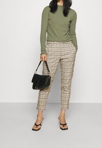Ribbad långärmad topp i olivgrön, i kombination med rutiga byxor i beige och brunt. Svart handväska med guldaccenter. Svarta sandaler med remmar.