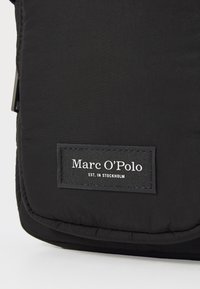 Borsa isolante nera con texture trapuntata, caratterizzata da un'etichetta in tessuto nero in rilievo con la scritta "Marc O'Polo" e "EST. IN STOCKHOLM."