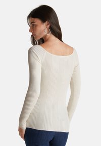 Gestreiftes Creme-Pullover mit langen Ärmeln und weitem Ausschnitt, aus einem strukturierten Stoff gefertigt, getragen zu dunkelblauen Denim-Jeans.