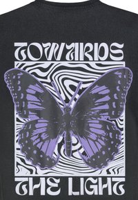 Schwarzes T-Shirt mit einer großen lila Schmetterlingsillustration mit kräftigen Umrissen, umgeben von wavy schwarz-weißen Mustern und dem Text "RICHTUNG LICHT".