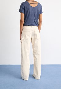 Haut bleu marine à manches courtes avec bretelles dans le dos ; pantalon cargo crème avec plusieurs poches ; tissu lisse et léger ; coupe décontractée ; position debout, vue de dos.