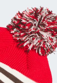 Rød strikket hue med en stor multicolor pom-pom på toppen, med hvide vandrette striber og et textured ribbet mønster.
