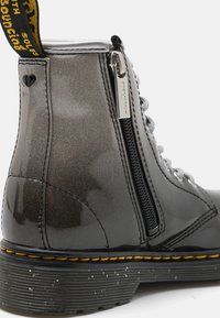 Stivaletto nero lucido con finitura testurizzata, zip metallica, lacci grigi e cuciture gialle a contrasto sulla suola. Passante in argento.