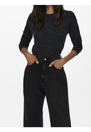 Schwarzer Strickpullover mit langen Ärmeln, rundem Ausschnitt und strukturierter Oberfläche, kombiniert mit hochgeschnittenen schwarzen Jeans mit Fronttaschen.