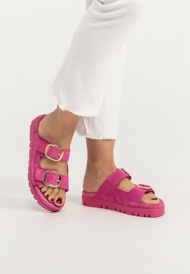 Pink suede buckle sandals with a chunky rubber sole and wide straps. Features two large buckles. Worn with white cropped pants.