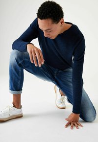 Camisa de manga larga navy, jeans azules y zapatillas blancas con suela de goma. La textura de la camisa es suave; los jeans tienen puños enrollados y un corte relajado.
