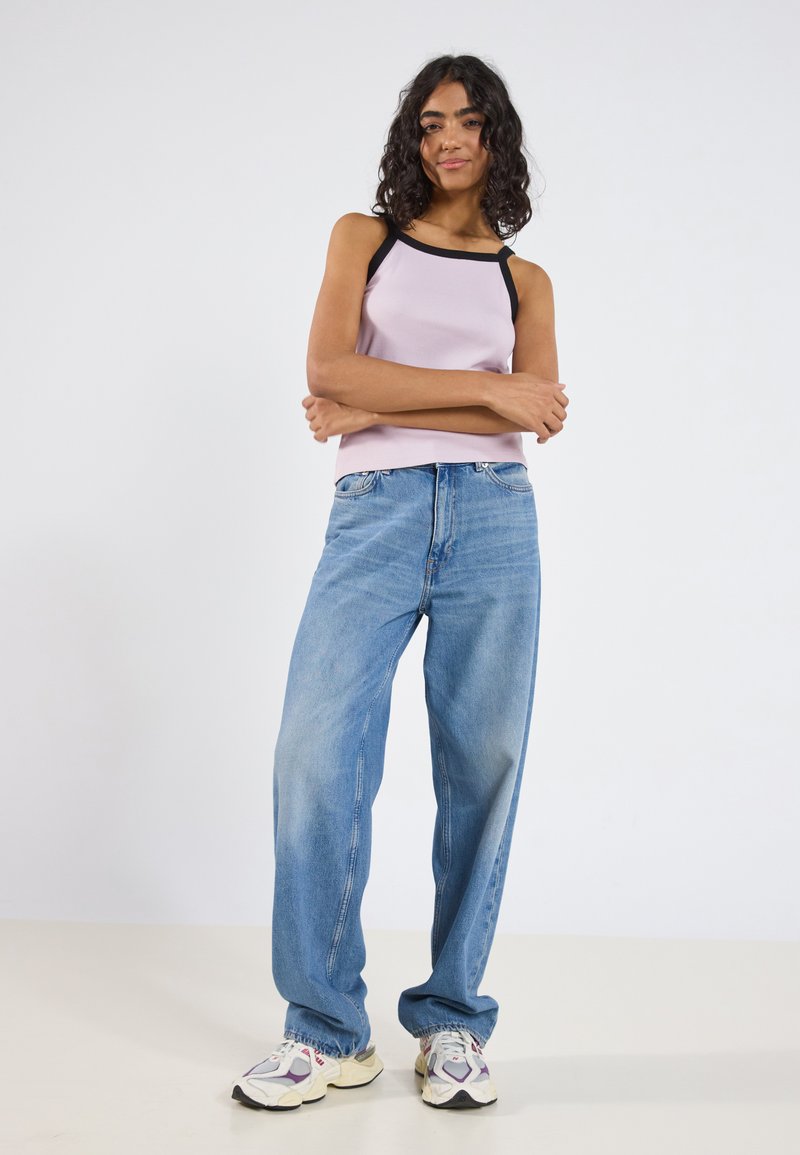Lys lilla ribbete tanktop med svarte stropper, kombinert med løse blå denimjeans og grå-hvite sneakers med multicolor detaljer.