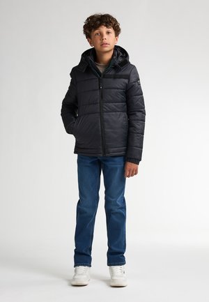 Zwarte pufferjack met een capuchon, voorzien van een rits aan de voorkant, zijzakken en geribbelde manchetten, gecombineerd met blauwe denim jeans en witte sneakers.