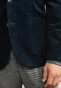 Granatowa marynarka z korduroju w pionowe prążki, z kieszonką i guzikami, w zestawieniu z spodniami w szare i czarne wzory houndstooth.