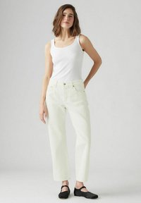 Witte geribbelde tanktop gecombineerd met lichtbeige hoge taille recht gesneden jeans, met klassieke zakken en een slanke zwarte sandaal.