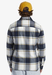Flanellskjorta i marinblått, vitt och beige rutmönster. Inkluderar klassisk krage och knäppta ärmslut. Mjuk textur och avslappnad passform.