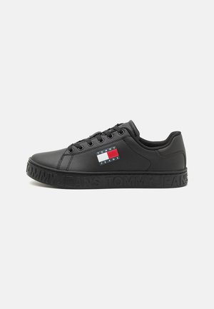 Black synthetic sneakers with flat rubber sole, lace-up design, and embossed "TOMMY JEANS" branding on the side. Features a small logo patch.