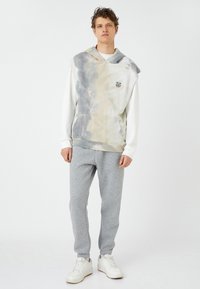 Lichte grijze hoodie met tie-dye, voorzien van een kangoeroe zak en logo. Gecombineerd met grijze tapered joggingbroeken en witte sneakers.