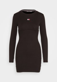 Long-sleeve black dress with a round neckline, ribbed texture, fitted design, and a contrasting logo patch on the upper chest.