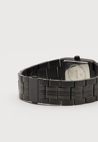 Μαύρο μεταλλικό ρολόι χειρός με τετράγωνο καντράν, γυρισμένο ώστε να φαίνεται η πίσω πλευρά και κούμπωμα με χαραγμένο το "BOSS".