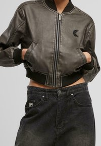 Veste bomber en cuir gris foncé avec des poignets et un col côtelés, avec une fermeture éclair à l'avant et deux poches latérales. Associée à un jean en denim foncé.