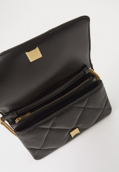 Mala de mão de couro acolchoado preta com ferragens douradas, apresentando uma aba superior, compartimentos interiores e um bolso com fecho.