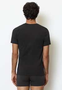Sort bomuldstrøje med rund hals og korte ærmer, der har en glat tekstur og et enkelt design, båret med matchende mørke shorts.
