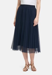 Donkerblauwe geplooide tule rok met een elastische tailleband. Doorzichtige overlay reikt tot halverwege de kuit, gelaagd over een effen onderlaag.