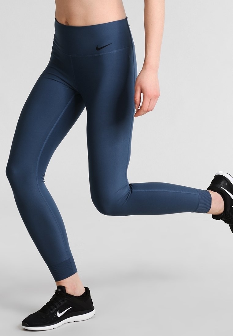 Leggings de sport navy en tissu extensible et lisse ; taille haute, coupe ajustée et logo discret sur la hanche gauche.