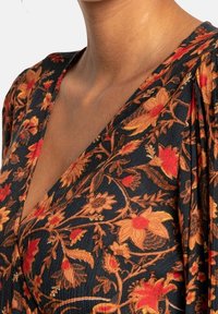 Robe à motif floral bleu foncé, ornée de fleurs rouges et jaunes vives, avec un profond décolleté en V et des manches froncées. Tissu texturé.